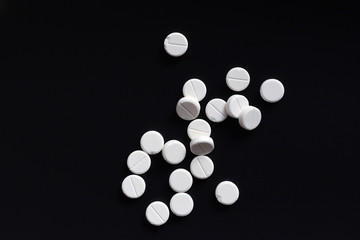 White round tablet pills placed at random on black background. Some of them have chipped edges. Top...