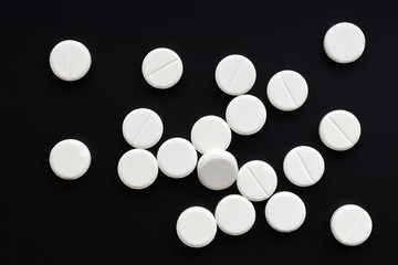 White round tablet pills placed at random on black background. Top view. Flat lay