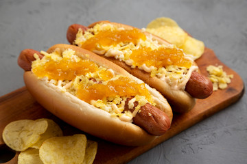 Homemade colombian hot dogs with pineapple sauce, chips and mayo ketchup on a rustic wooden board on a gray background, side view. Close-up.
