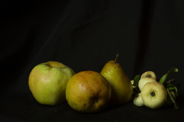  An apple, two pears and small wild apples on a black background, autumn still life