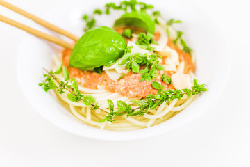Italian pasta with chopsticks, tomato sauce, parmesan cheese, fresh oregano and basil - on white background.