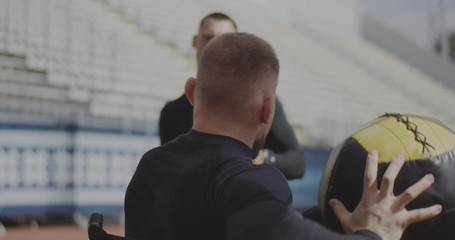 Wheelchaired athlete and trainer throwing medicine ball