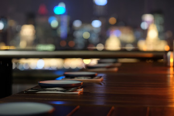 close up plates and cutlery in a row on outdoor restaurant table at night. Blur colorful city lights background.