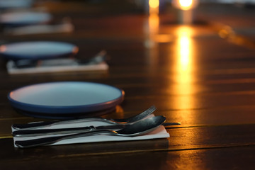 Obraz na płótnie Canvas close up plates and cutlery in a row on restaurant table at night. Shiny yellow light reflection on table