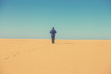 Fototapeta na wymiar A traveler is walking through the sandy desert. A man goes to the horizon. Wanderlust