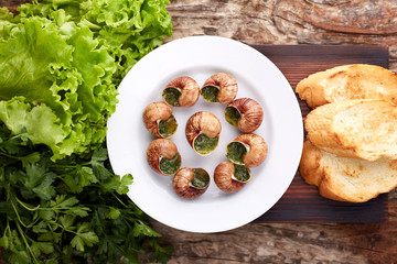 Escargots de Bourgogne - Snails with herbs butter on wooden background. Salad. Parsley.