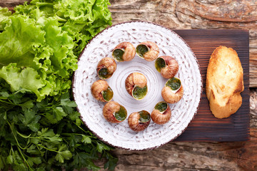 Escargots de Bourgogne - Snails with herbs butter on wooden background. Salad. Parsley.