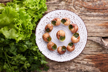 Escargots de Bourgogne - Snails with herbs butter on wooden background. Salad. Parsley.