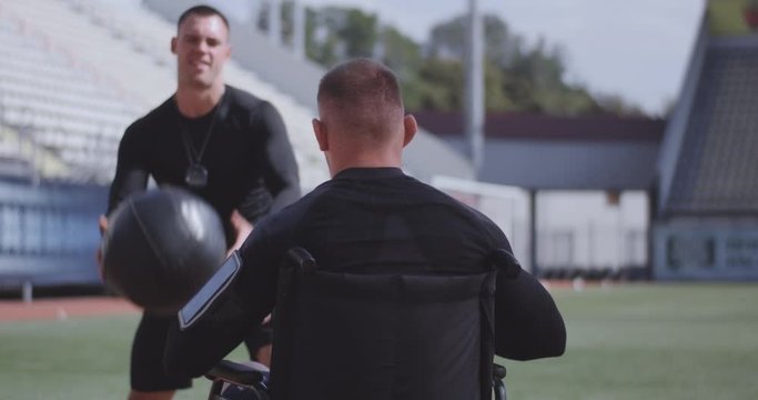 Wheelchaired athlete and trainer throwing medicine ball