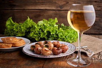 Escargots de Bourgogne - Snails with herbs butter on wooden background. Salad. Parsley. Glass of wine.