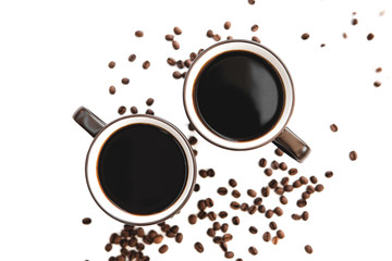 two large mugs of dark color with light walls and dark inside brewed coffee, standing on a light table where chaotically scattered roasted coffee beans