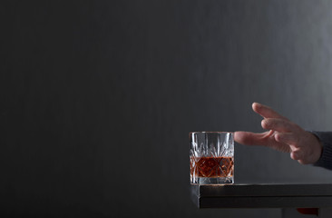 Man's hand reaches for a glass of alcohol.