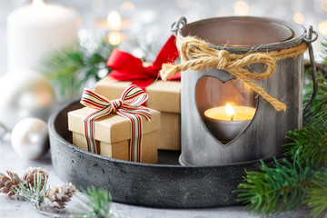 Merry Christmas greeting card with a rustic shabby chic lantern, festive gift with beautiful bows and lit candles, baublea and fir branches at the background