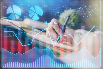 Financial forex graph displayed on hands taking notes background. Concept of research. Multi...