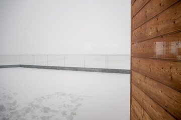 Wooden wall on terrace covered by snow at cable car station Birg on Schilltorn mountain with foggy background and copy space