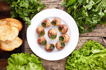Escargots de Bourgogne - Snails with herbs butter on wooden background. Salad. Parsley.