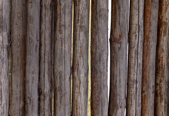 Background texture of a wooden fence of logs. Brown logs interconnected vertically. Cropped shot, horizontal, close-up. Concept of design and construction.