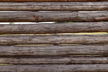 Background texture of a wooden fence of logs. Brown logs interconnected horizontally. Cropped shot, horizontal, close-up. Concept of design and construction.