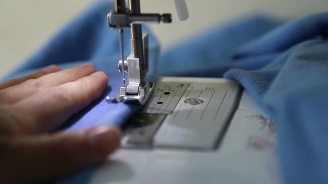 Woman stitching fabric on sewing machine. Hand and sewing process close-up.