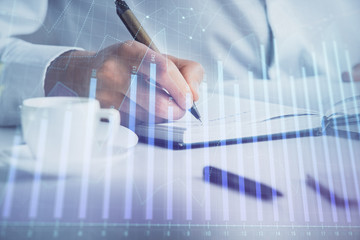 Double exposure of man's hands writing notes of stock market with forex chart.