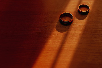 Female wedding frosted corrugated gold ring lie on male pair ring at the bottom of the white wooden...