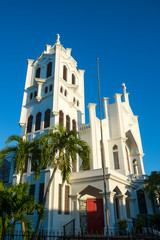 Bright scenic view of St. Paul's Episcopal church (built 1919) in simple white concrete with palm trees in Key West, Florida, USA