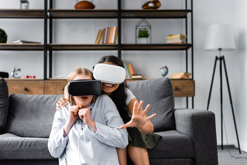 smiling multicultural friends with virtual reality headsets in apartment
