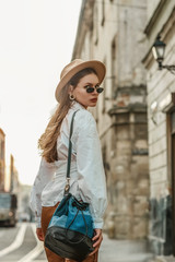 Outdoor fashion portrait of elegant, luxury woman wearing beige hat, black sunglasses, trendy white...