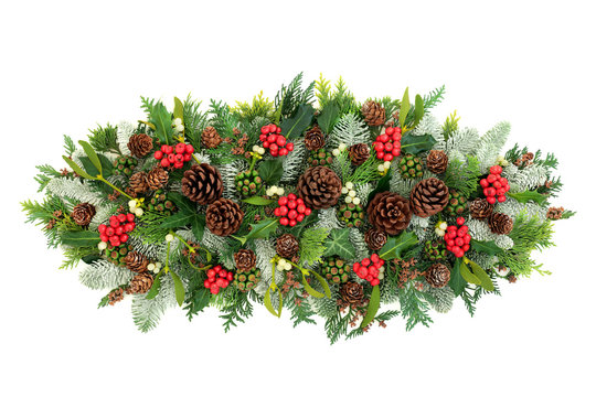 Winter and Christmas floral decoration with holly, snow covered spruce fir, mistletoe, cedar and ivy leaves with pine cones on white background with copy space.