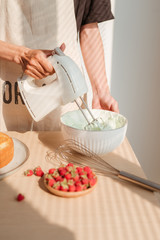 Male hands whipping whites cream in glass bowl with mixer on wooden table. Making sponge cake or red velvet cake