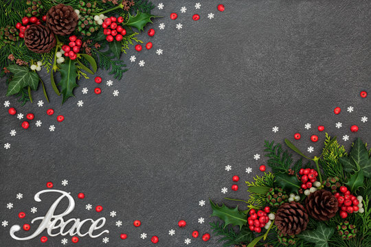 Christmas peace background border with silver sign and winter flora of loose holly berries and snowflake decorations on grunge grey background with copy space.