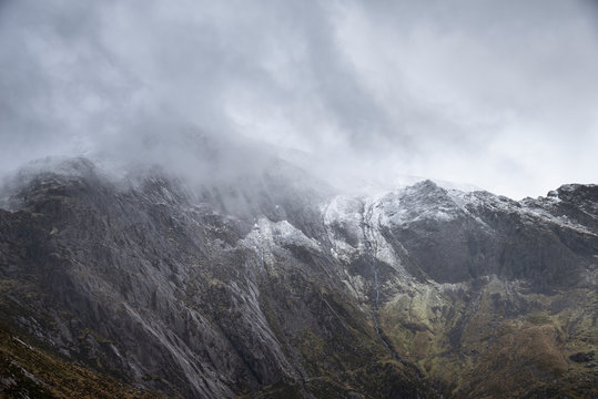 Stunning dramatic landscape image of snowcapped Glyders mountain range in Snowdonia during Winter with menacing low clouds hanging at the peaks