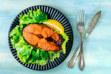 Fried salmon steak with greed salad leaves and lemon, shot from the top