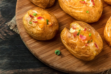 Naklejka na ściany i meble Baked potatoes with ham and green onion, close-up shot on a dark rustic wooden background with a place for text