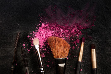 Make-up brushes with crushed cosmetics, shot from above on a black background with a place for text, a beauty design template for a makeup banner