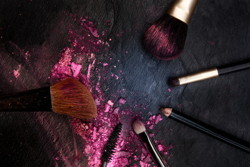 Make-up brushes with crushed cosmetics, shot from above on a black background forming a frame for copy space, a beauty design template for a makeup banner
