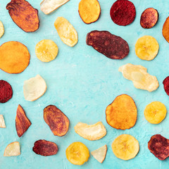 Dry fruit and vegetable chips on a teal blue background, forming a frame for copy space, overhead square shot