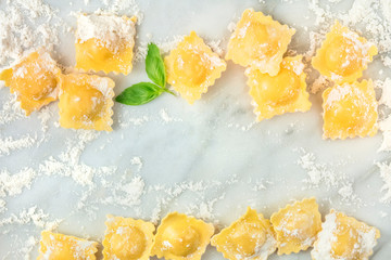 Ravioli with flour and basil leaves, forming a frame, shot from above on a white marble background with copy space, a design template for a recipe