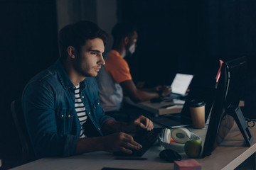 selective focus of young programmer working at night near african american colleague