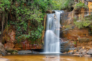 Idyllic waterfall with water motion blur n lush vegetation, red rock formations, Chapada dos Guimarães, Mato Grosso, Brazil, South America