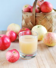 Fresh squeezed apple juice on wooden table, basket with ripe apples on background.