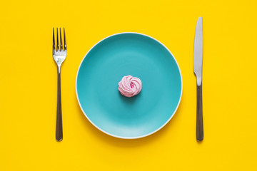 Flat lay  - Handmade pink marshmallows on color blue plate with fork and knife on yellow background.