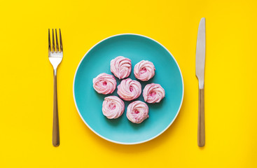 Flat lay  - Delicious and sweet desserts on color plate with fork and knife on yellow background. Handmade pink marshmallows.