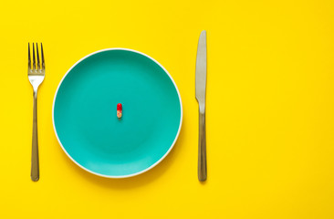 Colorful capsule on plate on yellow background with copy space. Health care or synthetic food concept. Top view.