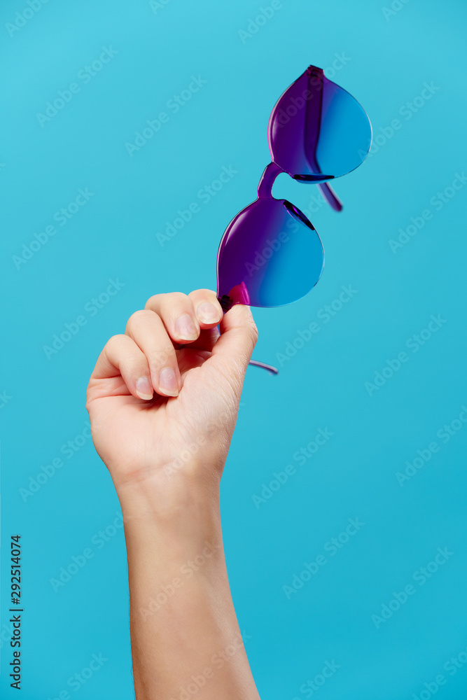 Wall mural image of hand with sunglasses on empty blue background