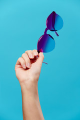 Image of hand with sunglasses on empty blue background