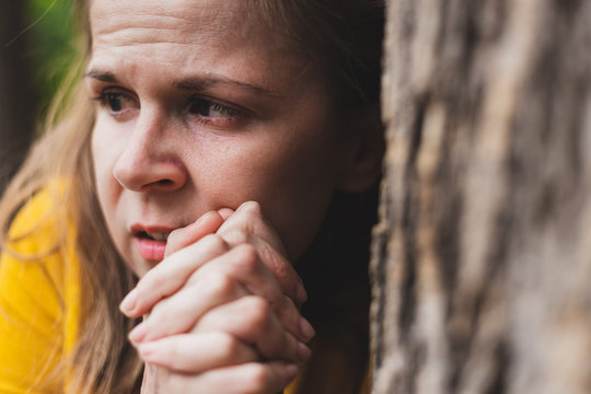 Close-up shot of a woman with paranoia hiding behind a tree