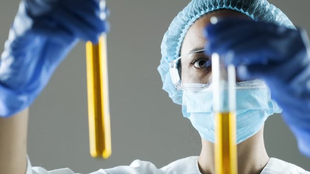 Chemical laboratory scene: attractive young PhD student scientist observing the engine oil or honey in the glass tube.
