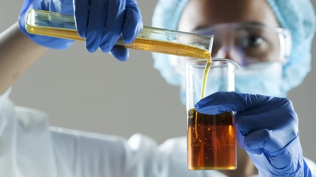 Chemical laboratory scene: attractive young PhD student scientist observing the engine oil or honey in the glass tube.