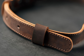 Brown belt made of genuine brown leather handmade on a dark background.